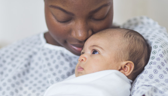 Beautiful African American mother in a hospital gown holds her newborn baby