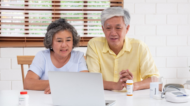 Asian couple seniors use laptop video conference with doctor about illness and prescription pill in living room at home